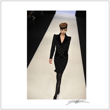 Model walking down the runway in a stylish black outfit with a fitted silhouette.