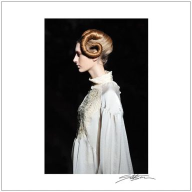 Profile of a model with an elaborate hairstyle and vintage gown against a dark background.