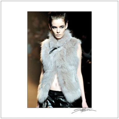 Model wearing a grey faux fur vest with a high collar on the runway.