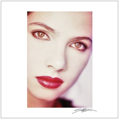 Close-up of a woman with striking brown eyes and red lips, featuring soft lighting.