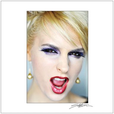 Woman with blonde hair, striking makeup, and a fierce expression, shouting passionately.