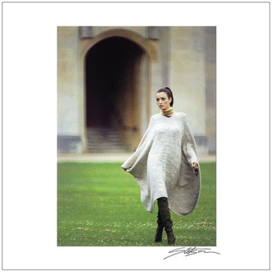 A woman in a flowing light sweater stands in a grassy area near an archway.