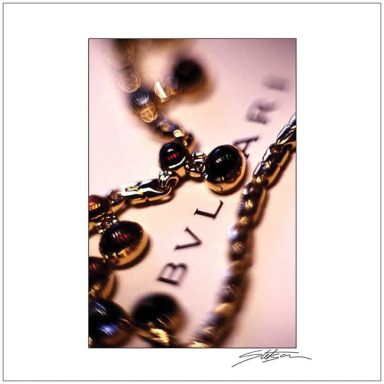 Close-up of a gold necklace featuring circular black stones and a Bvlgari logo in the background.